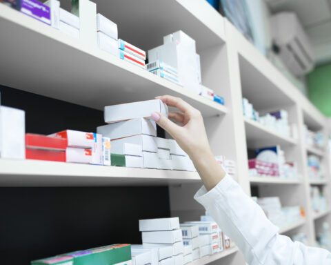 Closeup view of pharmacist hand taking medicine box from the shelf in drug store.
